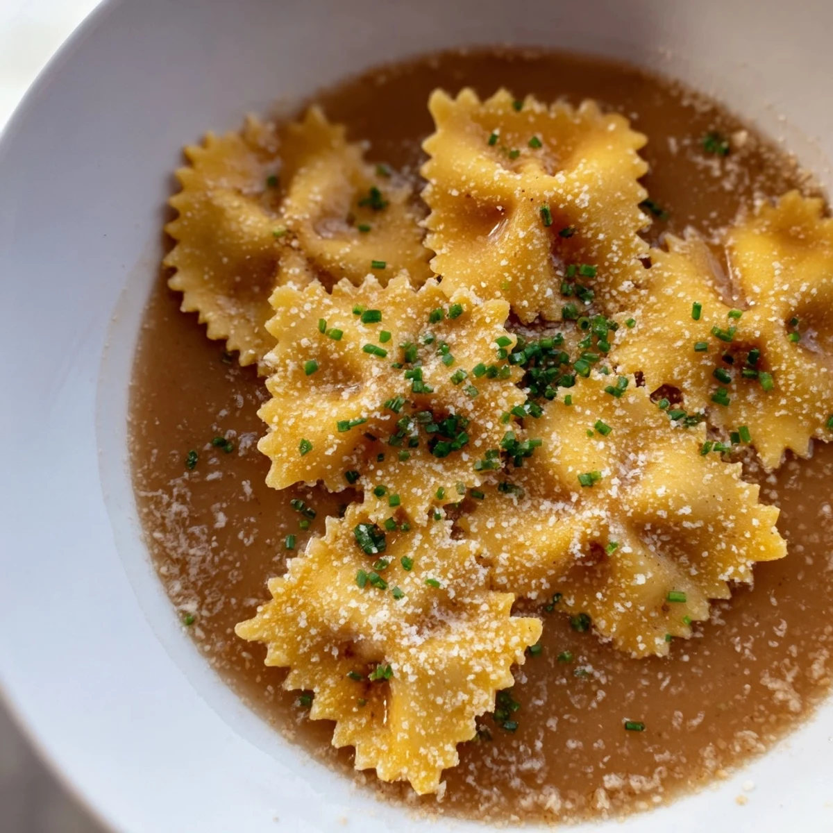 Crispy golden pasta chip cereal pieces in a bowl, swimming in flavorful parmesan broth.