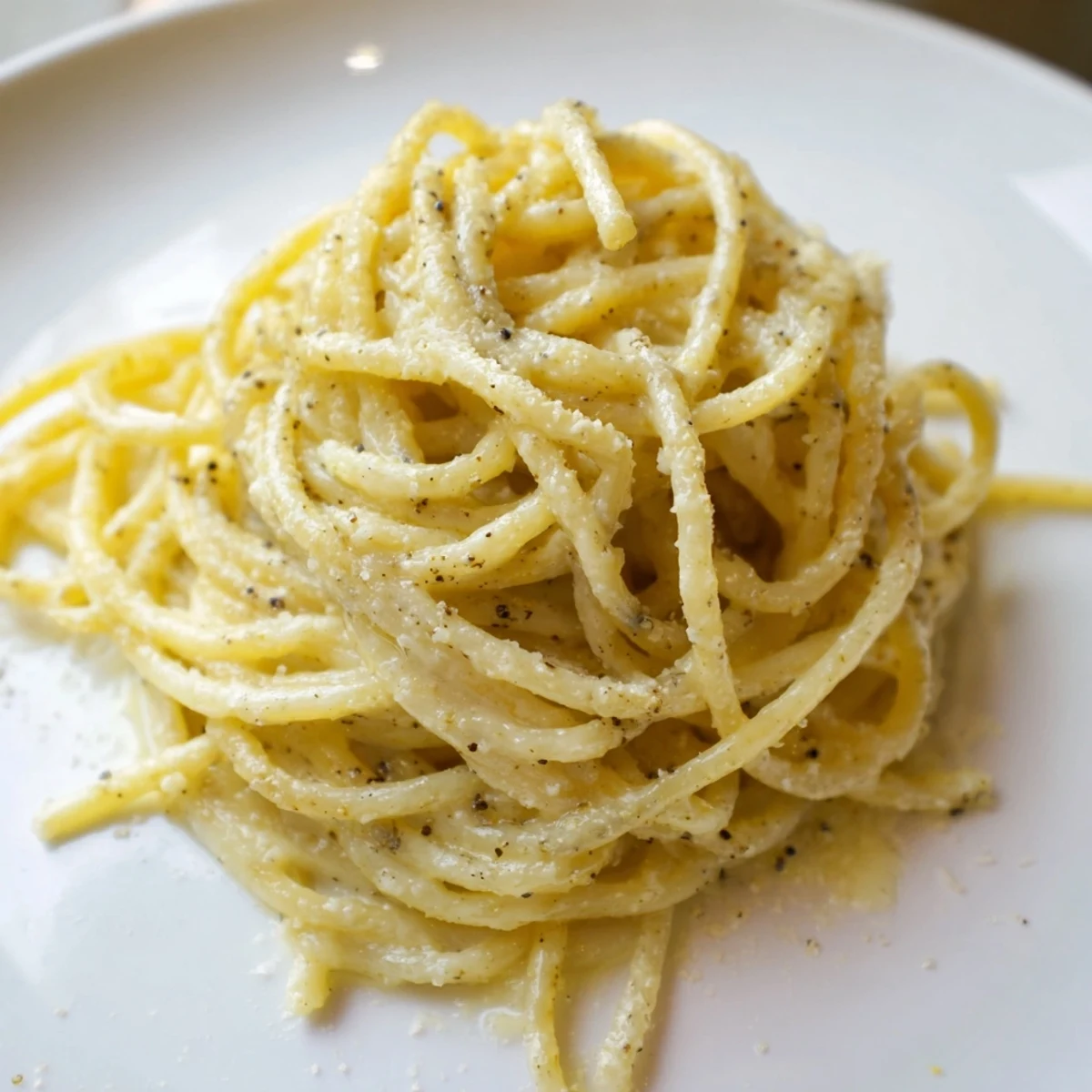 Golden strands of Spaghetti Cacio e Pepe glisten with a creamy, peppery sauce in a rustic skillet, ready to be served.  