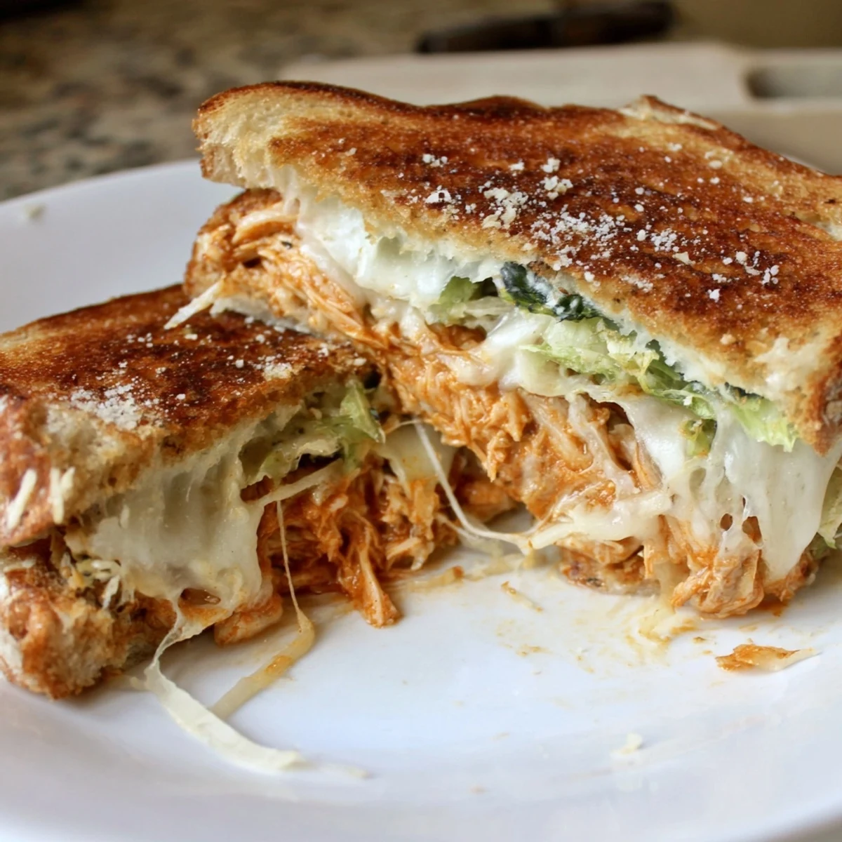A close-up of Buffalo Chicken Caesar Grilled Cheese, with melted provolone oozing from crispy sourdough slices.