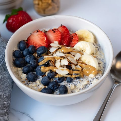 A jar of overnight oats with chia seeds, topped with fresh berries, sliced banana, and a drizzle of almond butter, ready to eat.
