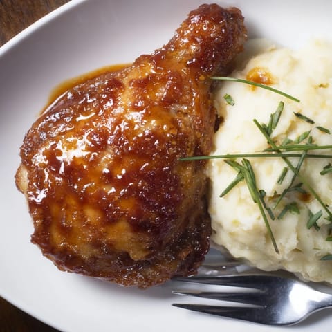 Oven-baked honey BBQ chicken thighs next to velvety garlic mashed potatoes, a delightful meal.  