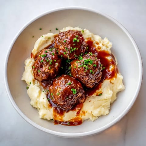 A close-up shot of rich, glossy BBQ Meatballs with creamy mashed potatoes, a comforting classic.
