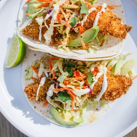 Warm corn tortillas hold the delicious crispy fish tacos, avocado, and creamy sauce; a treat!