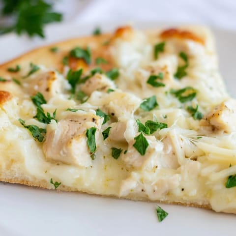 Fresh parsley tops a slice of homemade Chicken Alfredo Pizza, with rich cheese and savory chicken on a crisp, golden-brown crust.  