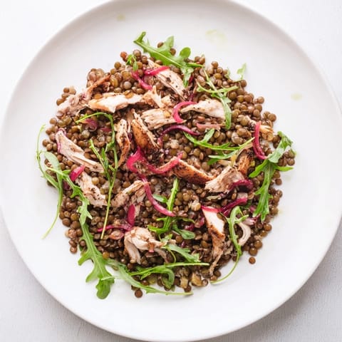 A close-up view of a colorful Lentil & Chicken Spring Salad featuring juicy cherry tomatoes and crisp cucumber slices on a rustic wooden table.  
