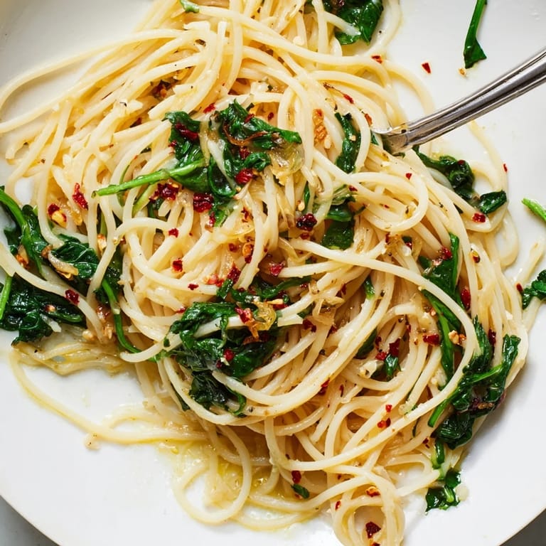 Deliciously simple Spaghetti Aglio e Olio adorned with fresh wilted spinach leaves.  