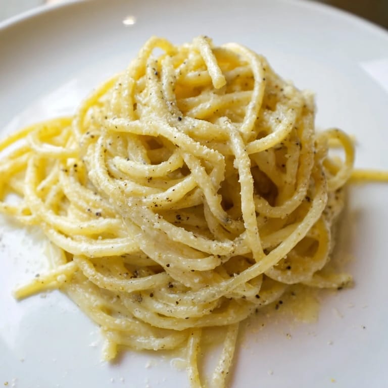 Golden strands of Spaghetti Cacio e Pepe glisten with a creamy, peppery sauce in a rustic skillet, ready to be served.  