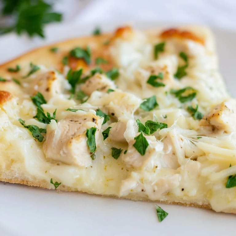 Fresh parsley tops a slice of homemade Chicken Alfredo Pizza, with rich cheese and savory chicken on a crisp, golden-brown crust.  