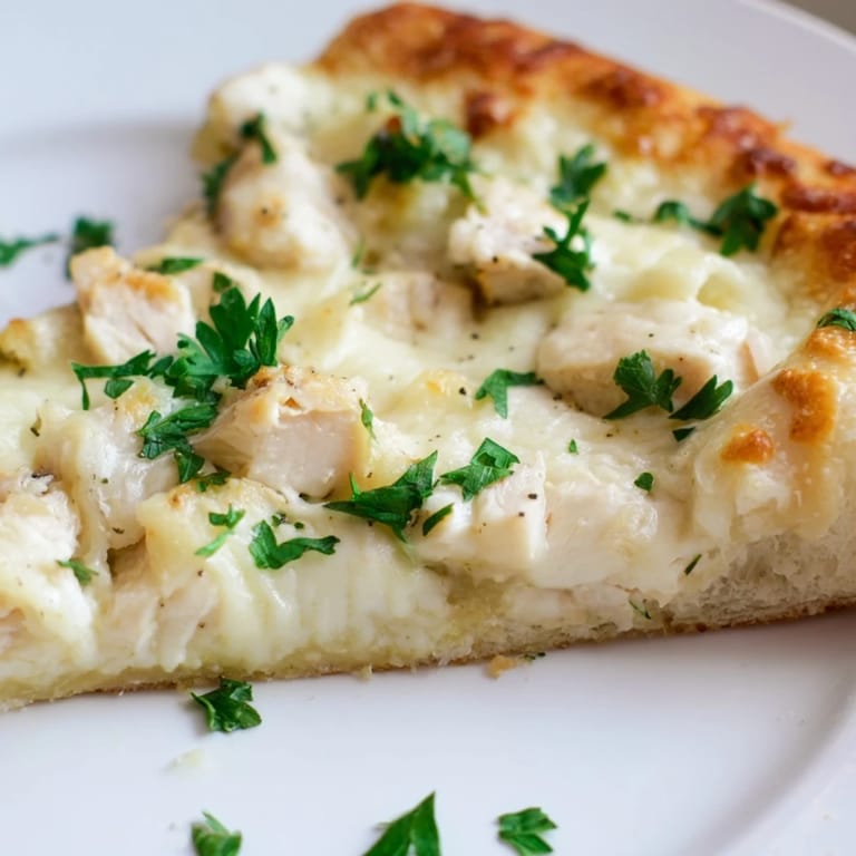 A hot Chicken Alfredo Pizza is sliced open, showing melted mozzarella and Parmesan over chicken, perfect for an Italian-American dinner.