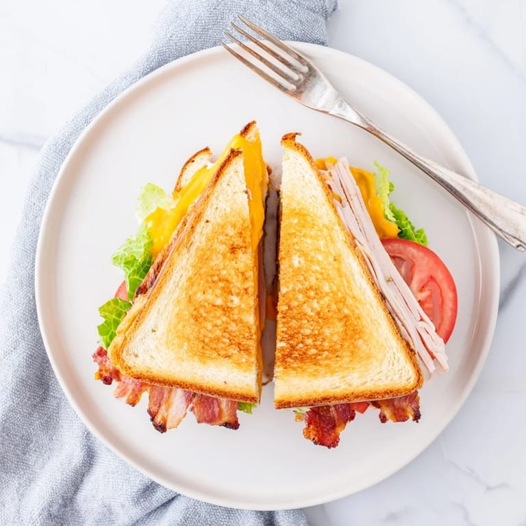 Buttery sourdough cradles the Turkey Club Grilled Cheese, with bacon and turkey peeking out beside a crisp salad garnish.